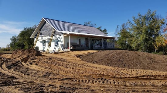 energy-efficient custom home under construction with a metal roof and insulated walls, surrounded by freshly graded land