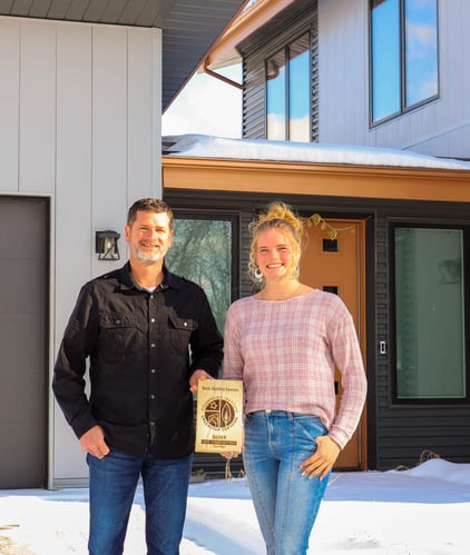 r-value homes jake and girl standing outside a modern energy-efficient custom home holding a silver award for sustainable construction